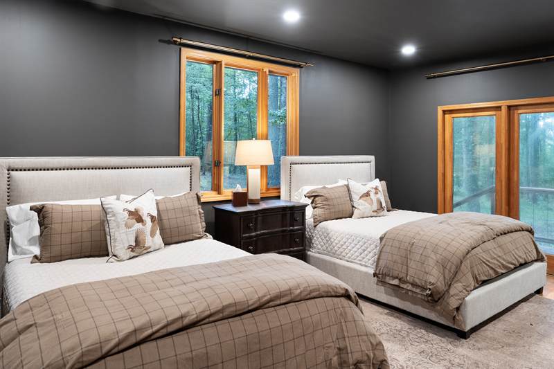 A bedroom with two twin beds and windows onto the woods