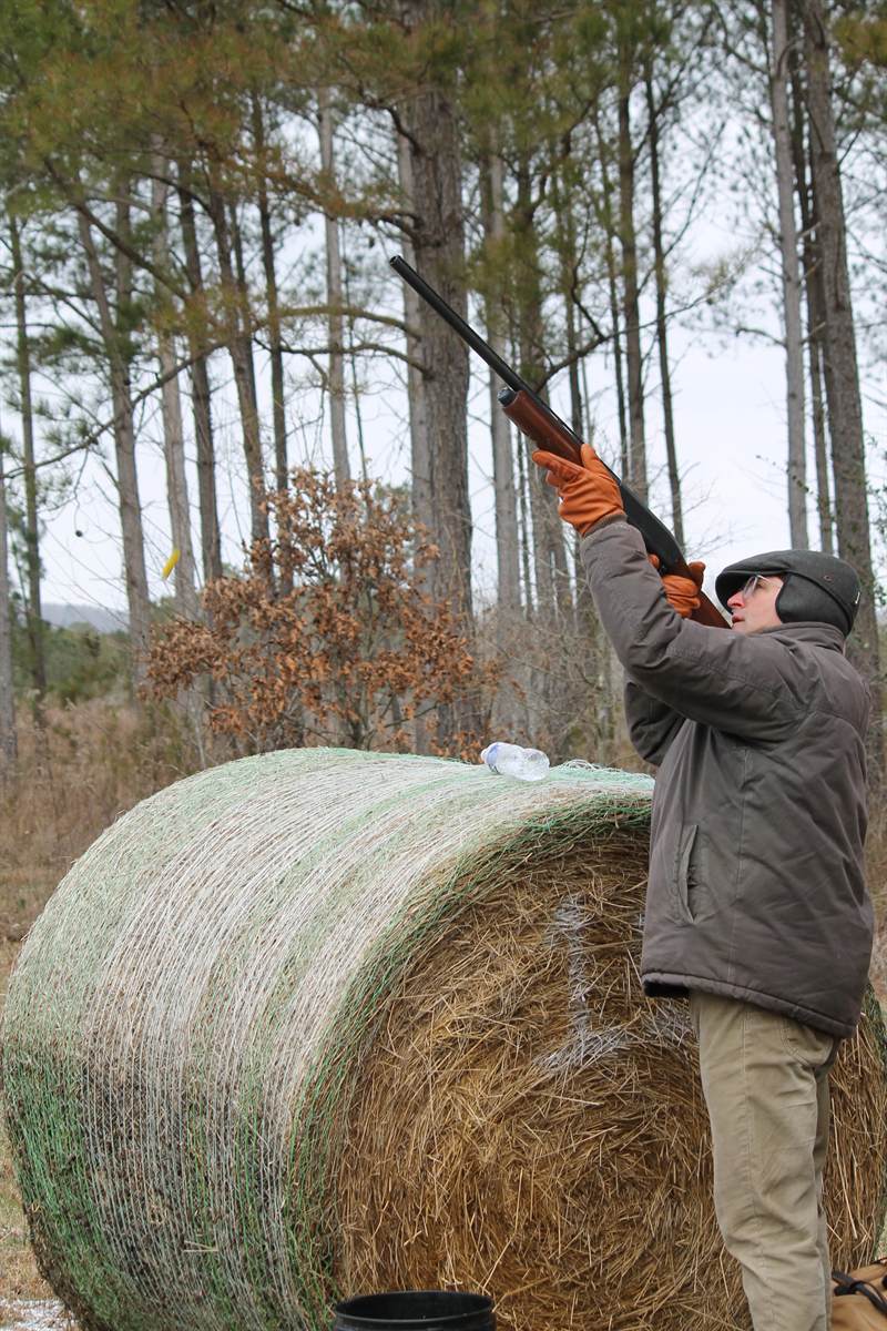 A shooter swinging on a bird beside a hay bale during falling snow