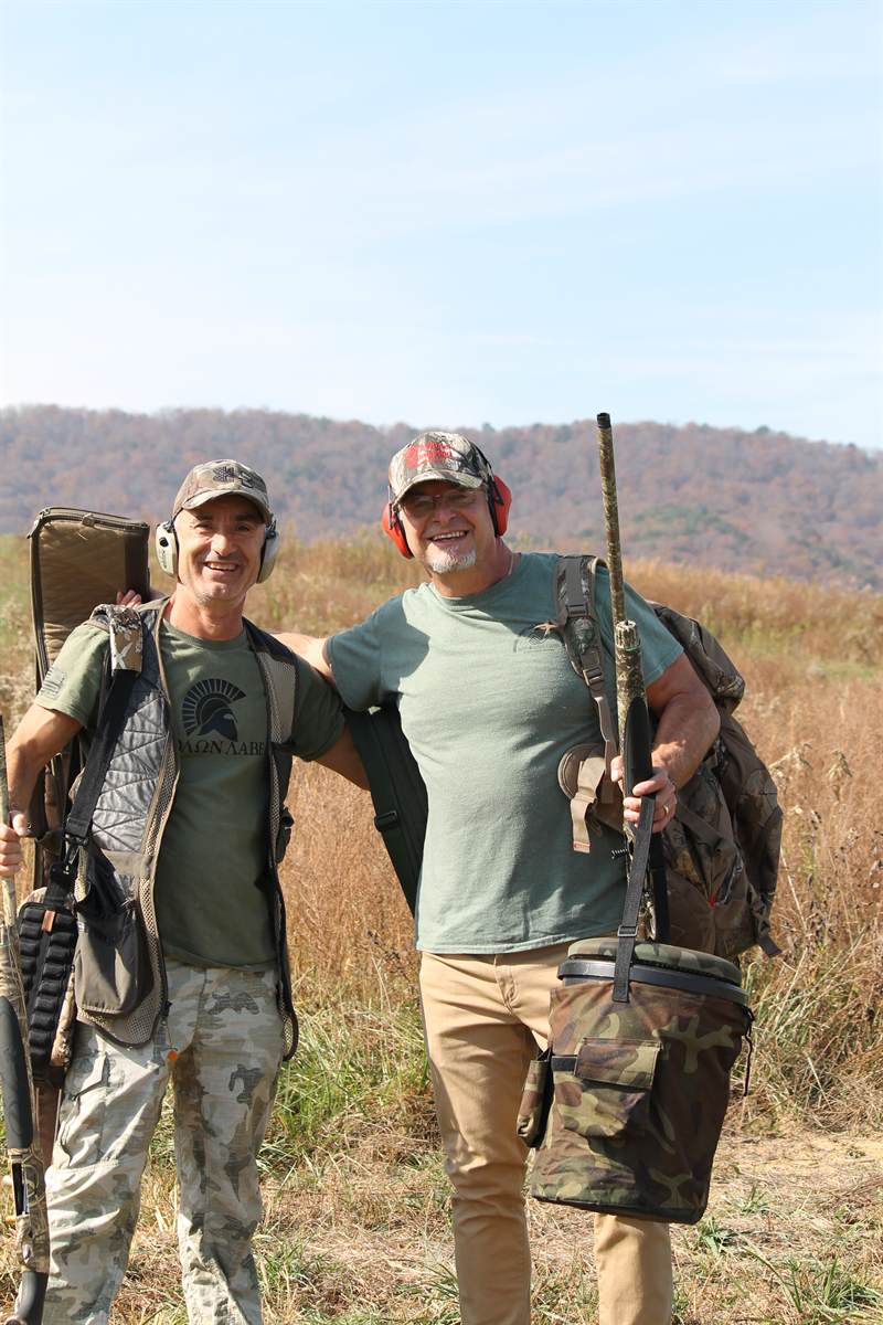 Two shooters walking out of the field with guns over their shoulders and a bag of birds
